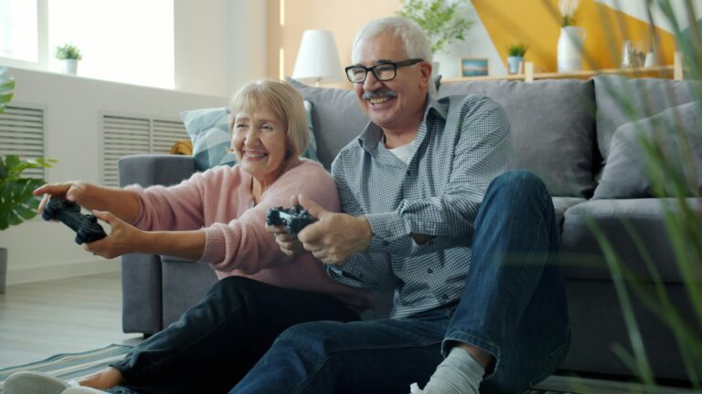 An older couple laughing over a video game on the sofa
