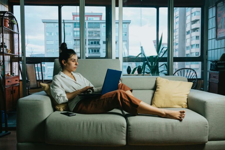 A woman relaxing with her laptop on a sofa by the windows