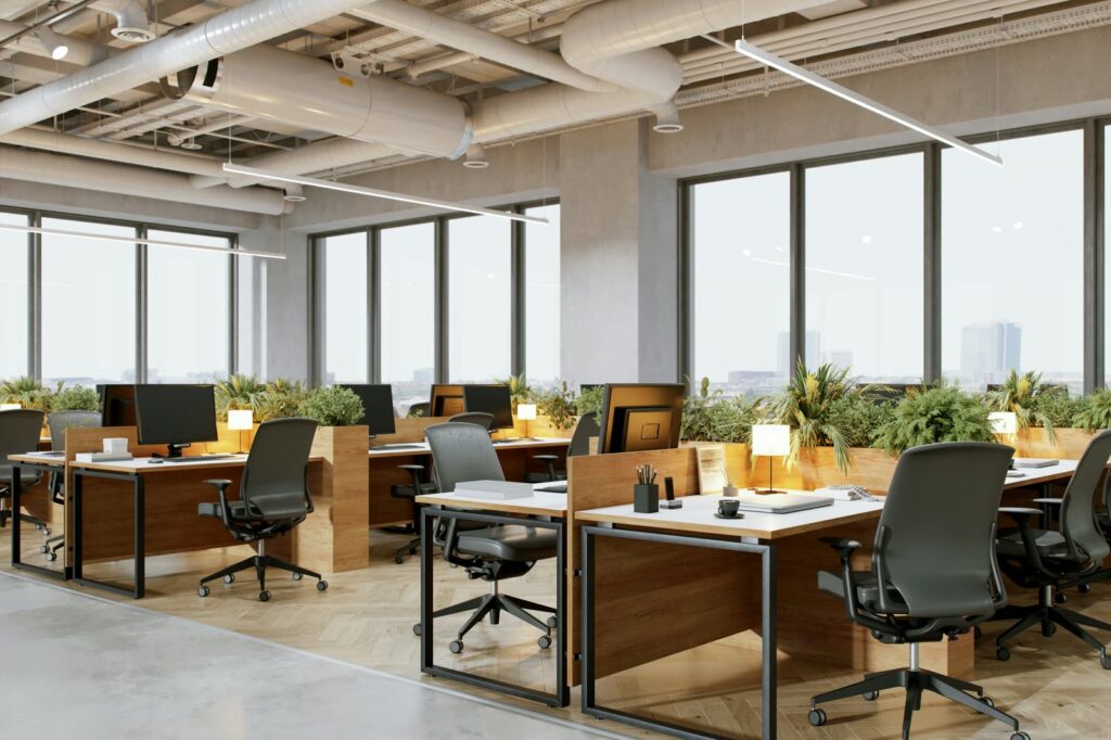 A bright open-plan office with wood desks, plants and tall windows