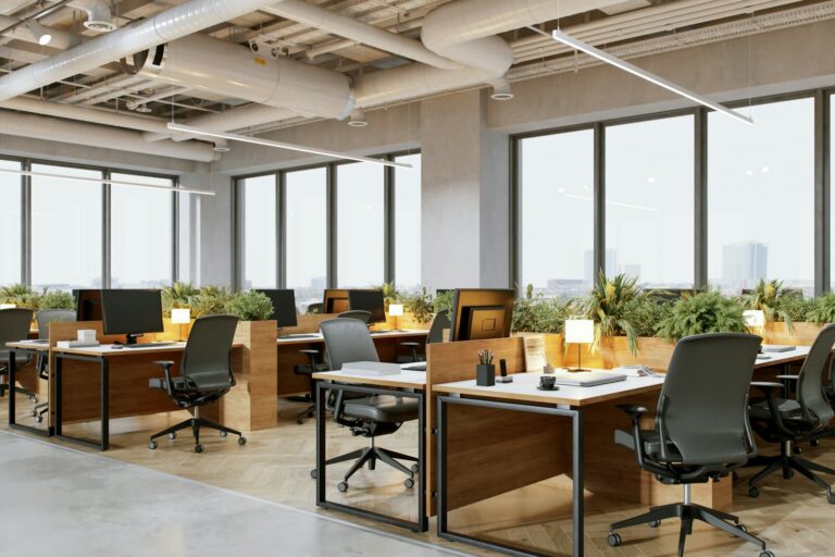 A bright open-plan office with wood desks, plants and tall windows