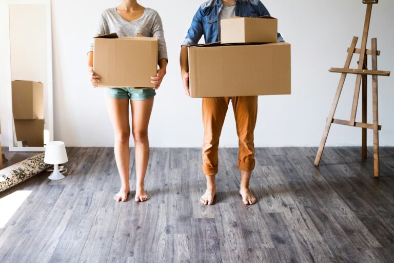 A couple carrying moving boxes into a bright, empty room