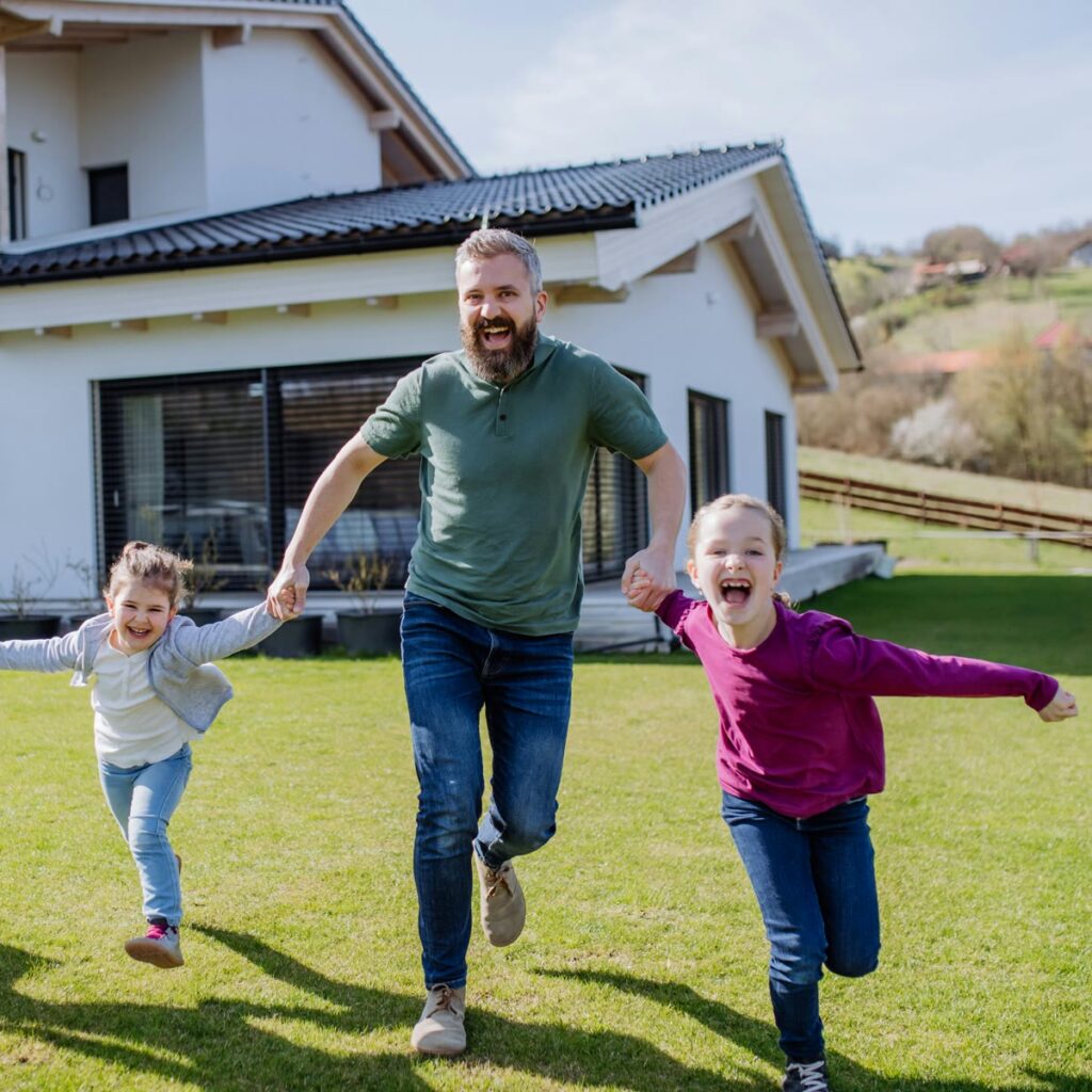 A father running hand in hand with his laughing daughters across a sunlit lawn